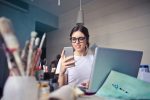 Девушка со смартфоном и ноутбуком за рабочим столом
